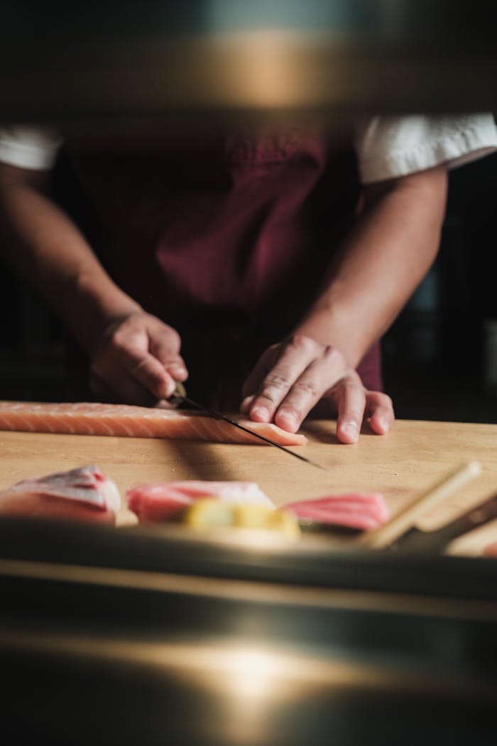 A chef skillfully slicing fresh salmon for sushi preparation on a wooden table.