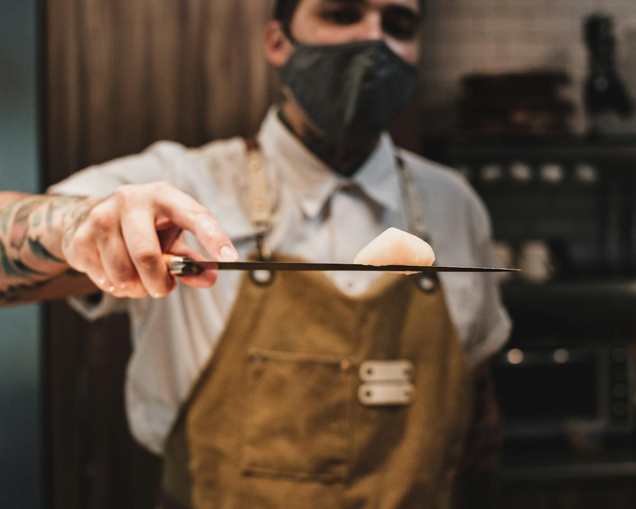 Chef with a face mask skillfully handles a sushi knife indoors.